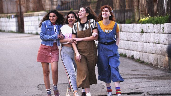 Filmstill aus MEMORY BOX. Vier junge Frauen gehen lachend und untergehakt eine Straße entlang.