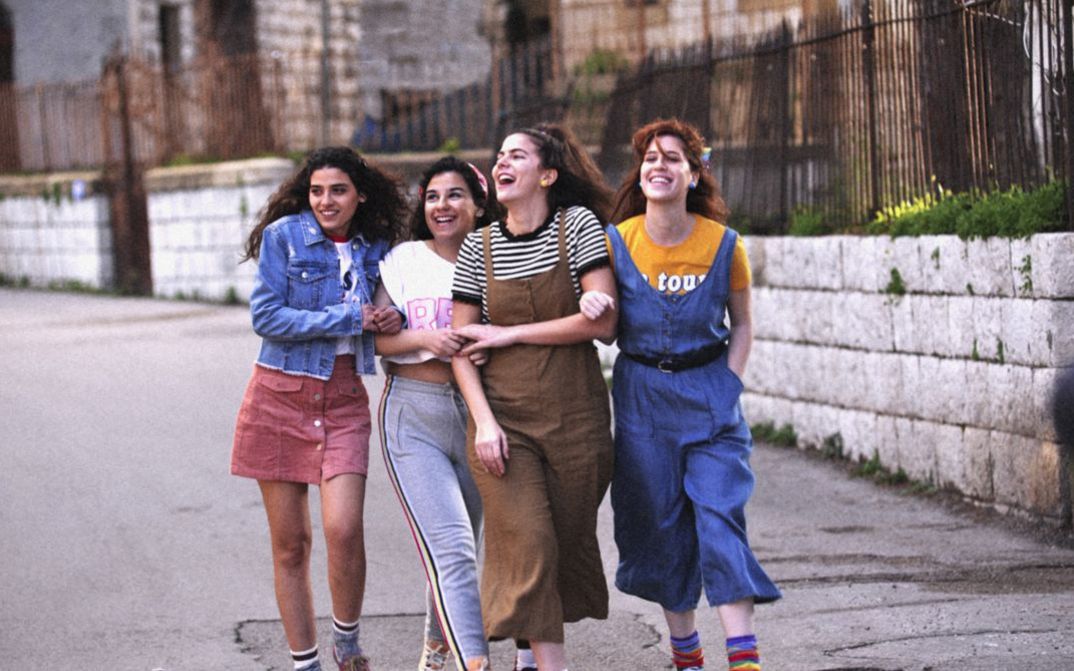 Filmstill aus MEMORY BOX. Vier junge Frauen gehen lachend und untergehakt eine Straße entlang.