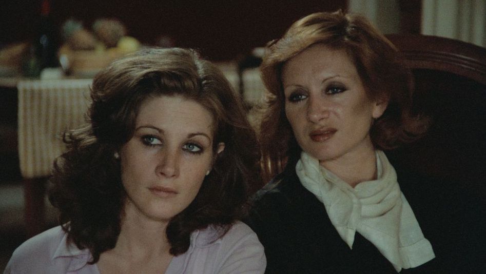 Filmstill aus SALE HISTOIRE: Zwei Frauen sitzen an einem Tisch und hören jemandem zu.