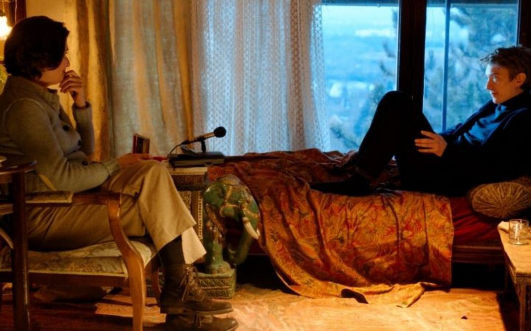 Filmstill aus VOUS NE DÉSIREZ QUE MOI: Ein Mann und eine Frau sitzen einander zugewandt in einem Zimmer, zwischen ihnen steht ein Mikrophon.