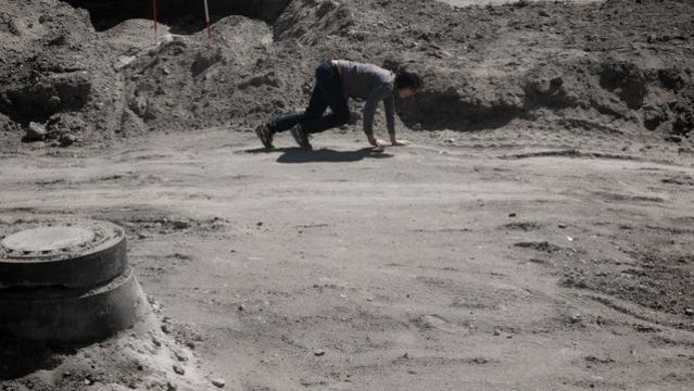 Filmstill aus F ZWISCHEN DEN STUFEN DES ORGANISCHEN: Ein Mann auf alle vieren zwischen Geröll.