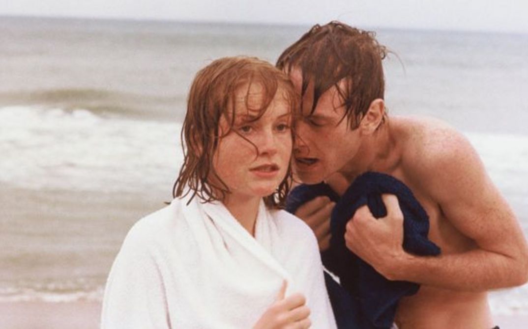 Filmstill aus LA DENTELLIÈRE: Ein junger Mann und eine junge Frau am Strand, er sagt ihr etwas ins Ohr.
