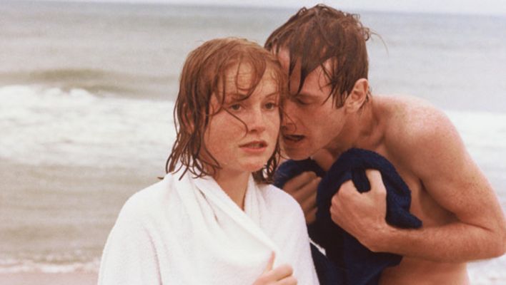 Film still from LA DENTELLIÈRE: A young man and a young woman on the beach, he says something in her ear.
