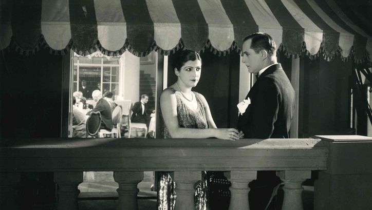 Filmstill aus DIE DAME MIT DEM TIGERFELL: Ein Mann und eine Frau in eleganter Abendkleidung stehen auf einer Terasse.