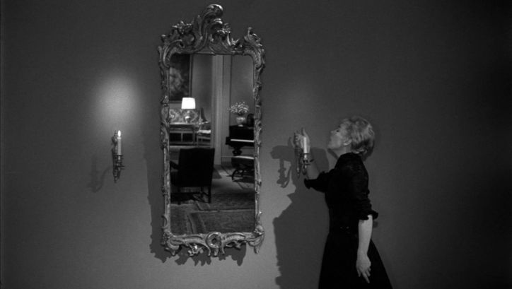 Film still from GERTRUD: A woman blows out a candle hanging next to a mirror.