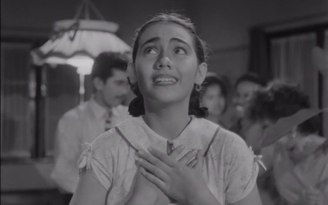 Film still from TIGA DARA: A young woman holds her hands in front of her chest and looks up.