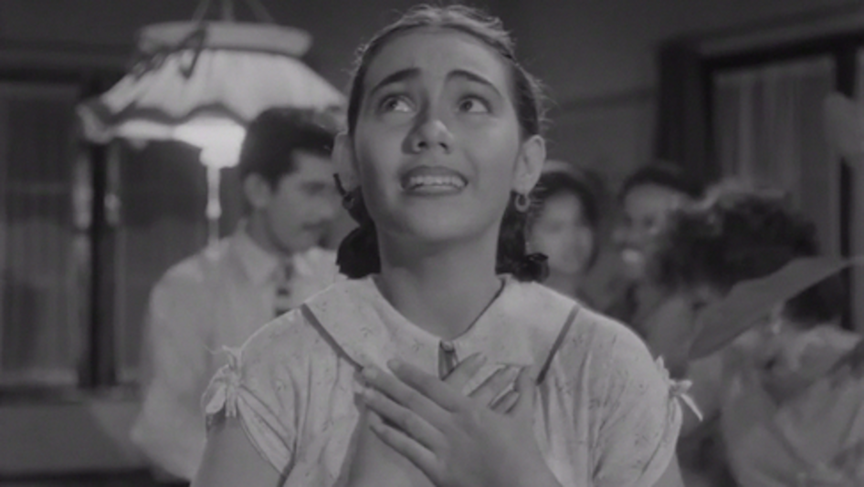 Film still from TIGA DARA: A young woman holds her hands in front of her chest and looks up.