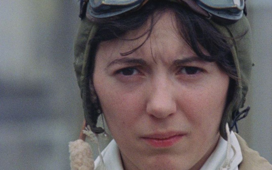 Film still from AMY: A woman wearing an aviator cap looks skeptically into the camera.