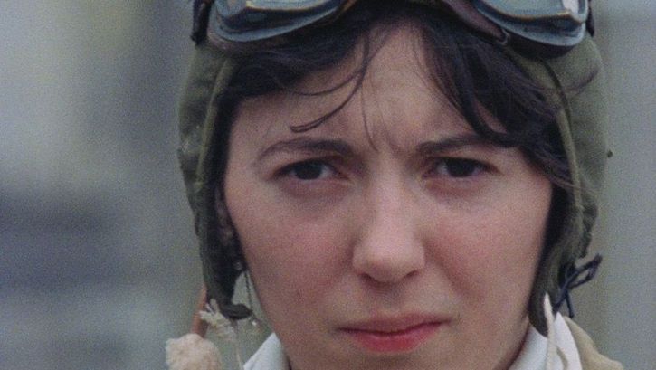 Film still from AMY: A woman wearing an aviator cap looks skeptically into the camera.