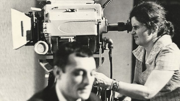 Film still from "Deda-Shvili an rame ar aris arasodes bolomde bneli" by Lana Gogoberidze. It shows a black and white image of a woman using a video camera. 