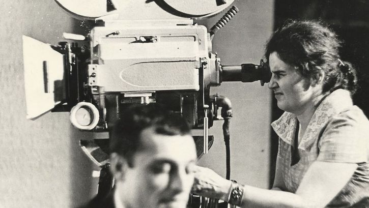 Film still from "Deda-Shvili an rame ar aris arasodes bolomde bneli" by Lana Gogoberidze. It shows a black and white image of a woman using a video camera. 