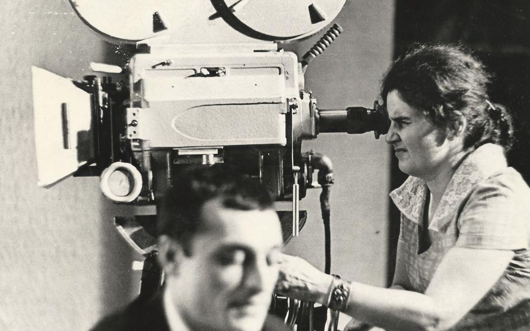 Film still from "Deda-Shvili an rame ar aris arasodes bolomde bneli" by Lana Gogoberidze. It shows a black and white image of a woman using a video camera.