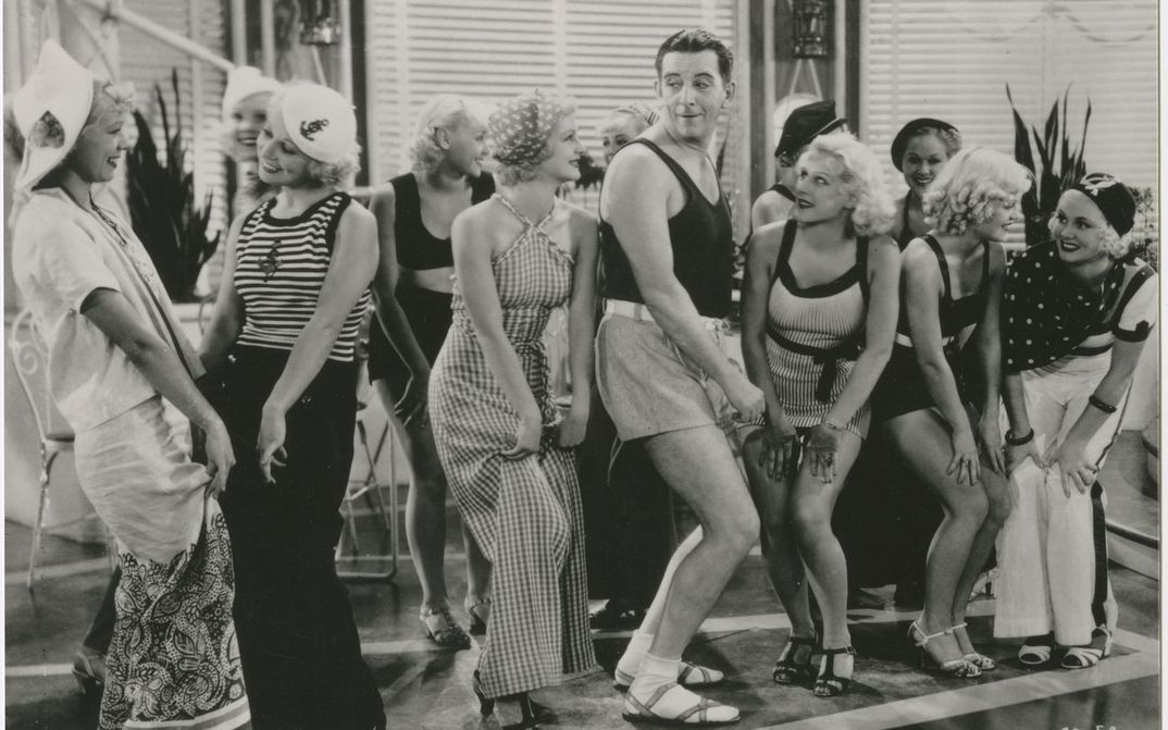 Filmstill aus THE GAY DIVORCEE: Edward Everett Horton ist in kurzen Hosen tanzend inmitten einer Gruppe von jungen Frauen.