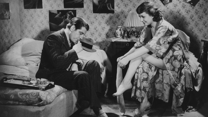 Filmstill aus LA BELLE ÉQUIPE: Ein Mann und eine Frau in einem Schlafzimmer. Er sitzt im Anzug auf dem Bett, sie sitzt ihm gegenüber in einem Bademantel und zieht sich Strümpfe an.