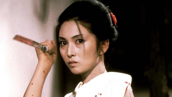 Film still from LADY SNOWBLOOD: A woman in a kimono holds a man spattered with blood in her hand. She is in attack position.