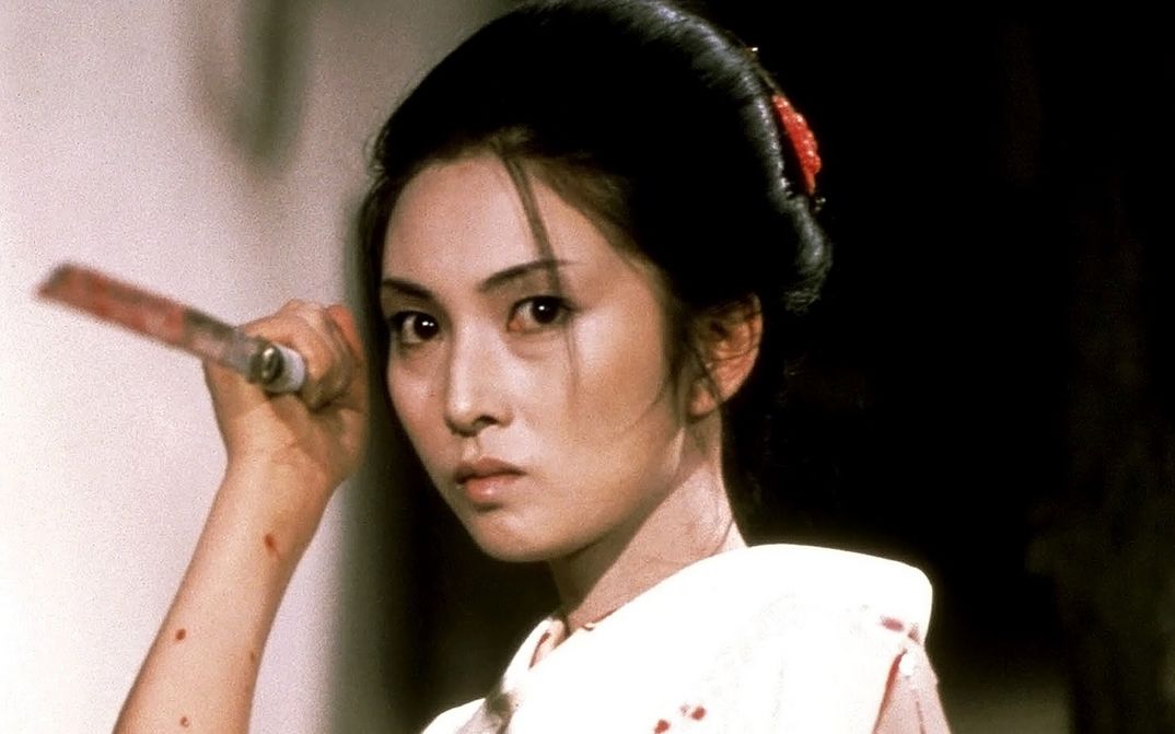 Film still from LADY SNOWBLOOD: A woman in a kimono holds a man spattered with blood in her hand. She is in attack position.