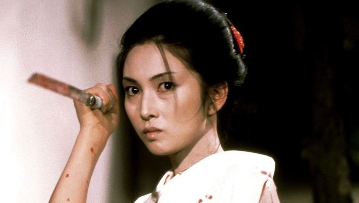 Film still from LADY SNOWBLOOD: A woman in a kimono holds a man spattered with blood in her hand. She is in attack position.