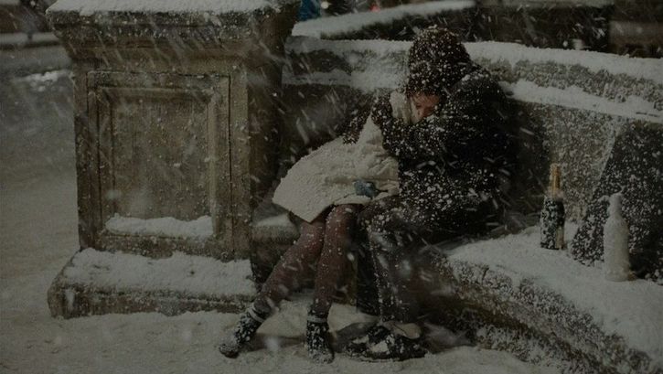 Film still from LES AMANTS DU PONT-NEUF: A couple embrace on a bench in the thick snow.