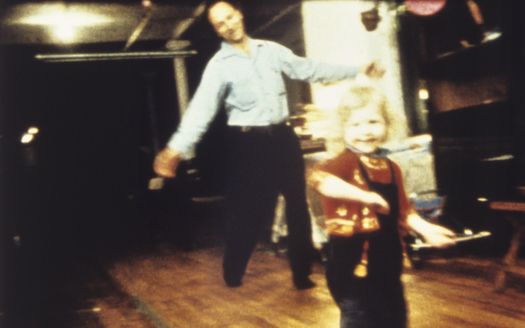 Filmstill aus PARADISE NOT YET LOST: Jonas Mekas und ein kleines Kind tanzen in einem Zimmer.
