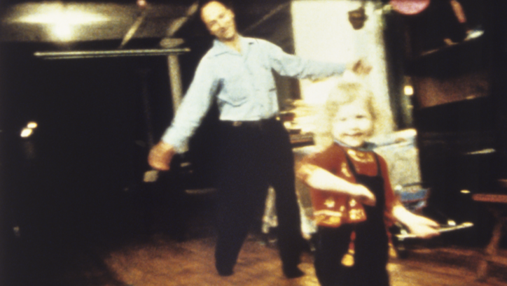Filmstill aus PARADISE NOT YET LOST: Jonas Mekas und ein kleines Kind tanzen in einem Zimmer.