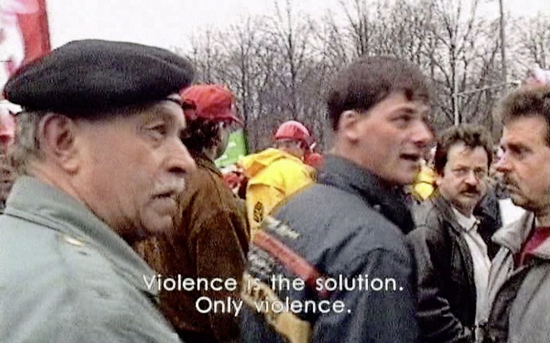 Still from the film "The Empty Center" by Hito Steyerl. People at a political demonstration. The subtitle says: Violence is the solution. Only violence. 