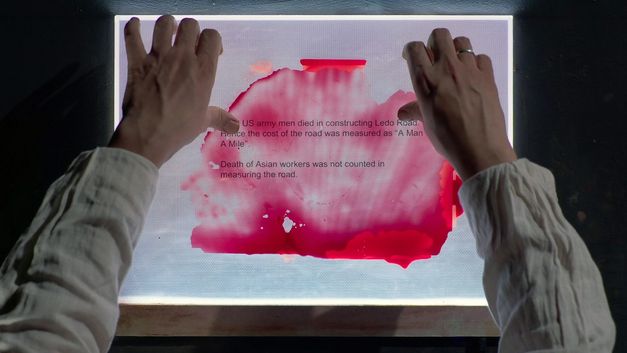 Hände halten Papier mit Text und roter Flüssigkeit auf Leuchttisch.