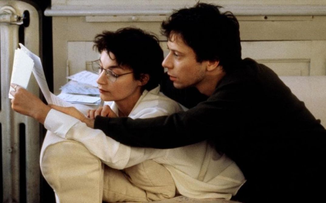 Film still from COMMENT JE ME SUIS DISPUTÉ .. (MA VIE SEXUELLE). A man and a woman lie on a sofa and read a manuscript together.