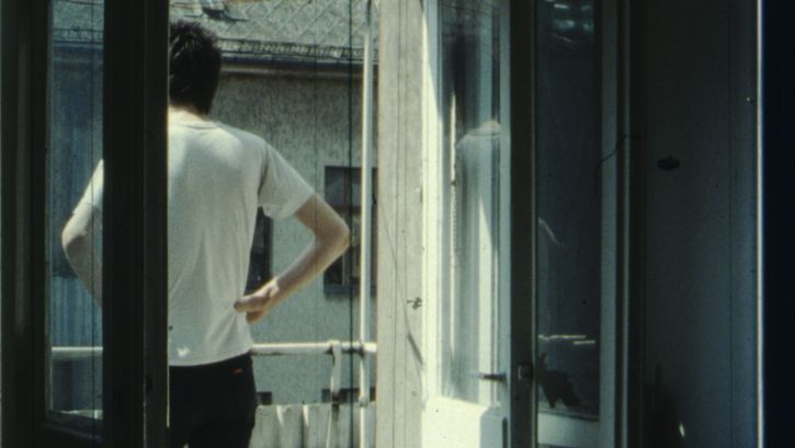 Film still from IM SOMMER: A person stands on the balcony with their hands on their hips.