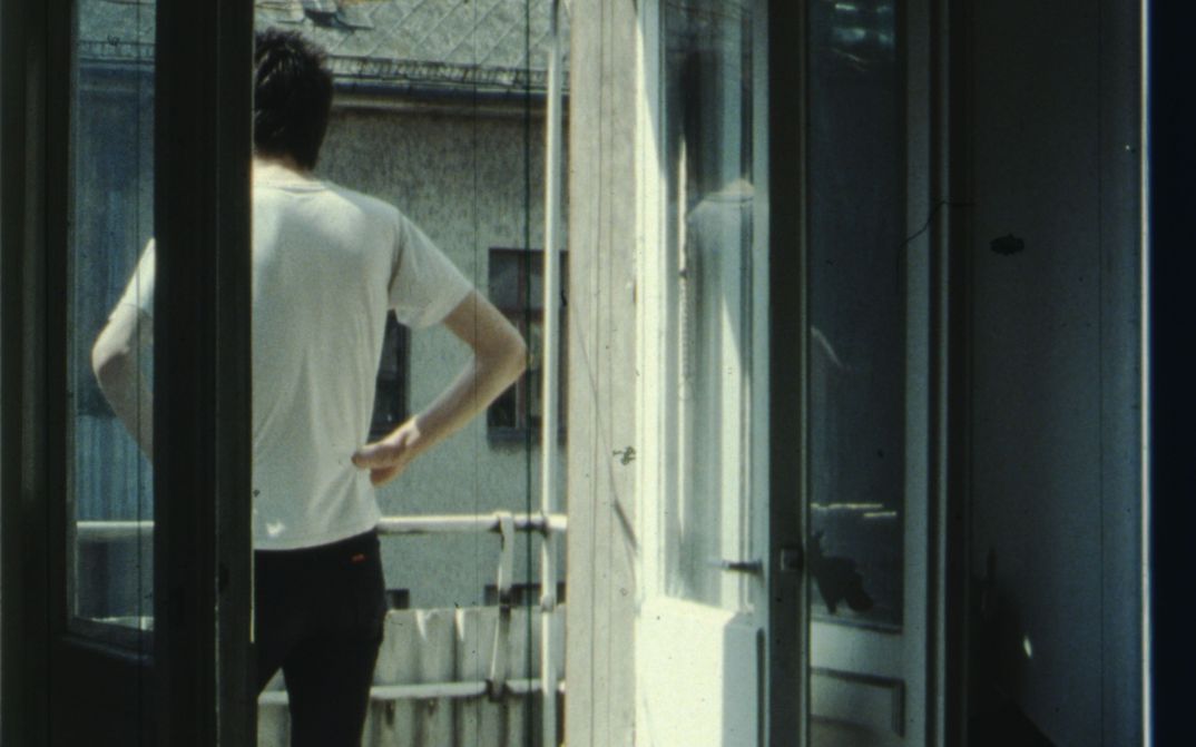 Film still from IM SOMMER: A person stands on the balcony with their hands on their hips.