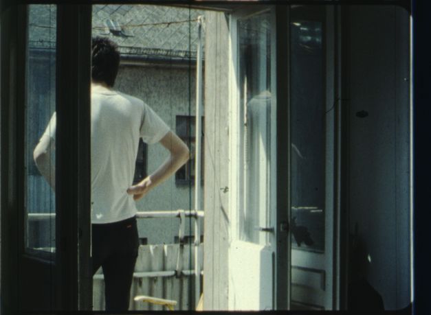Film still from IM SOMMER: A person stands on the balcony with their hands on their hips.