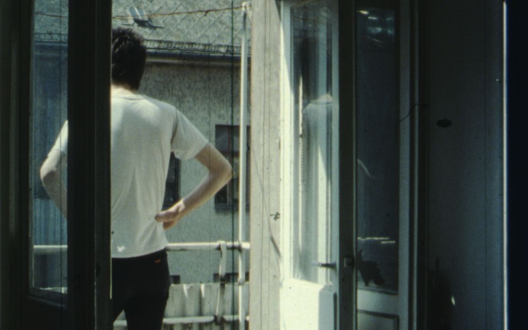 Film still from IM SOMMER: A person stands on the balcony with their hands on their hips.