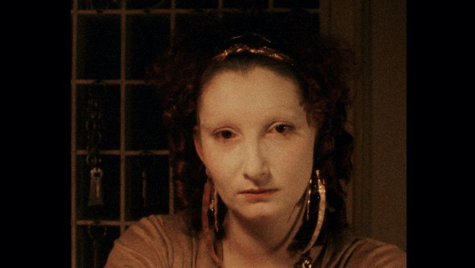 Filmstill aus NIGHTSHIFT: Eine junge Frau sitzt an der Rezeption eines Hotels und blickt frontal in die Kamera. Hinter ihr im Halbdunkel ist ein Schlüsselkasten zu sehen.