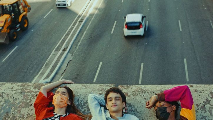 Filmstill aus TRES TIGRES TRISTES: Man sieht die Köpfe dreier junger Menschen auf einer Mauer. Hinter ihnen sind Autos auf einer Straße zu sehen.