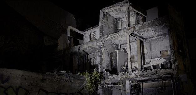 Filmstill aus "L’ homme-vertige" von Malaury Eloi Paisley. Zu sehen ist die Ruine eines Hochhauses bei Nacht. Die Ruine wird von einem weißen Lichtstrahl beleuchtet. 