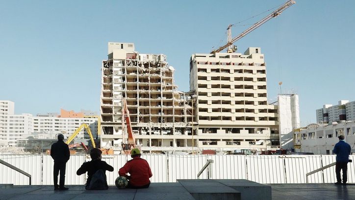 Filmstill aus BERLIN JWD: Ein paar Menschen sehen zu, wie ein Hochhaus abgerissen wird.