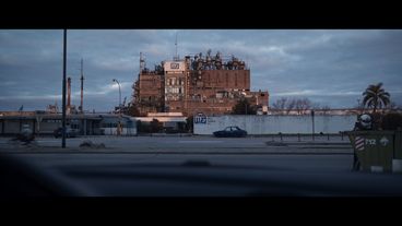 Panorama of a red factory building with the name "Manufactura de Fibras Sintéticas" on a white wall next to the factory gate, at dawn.