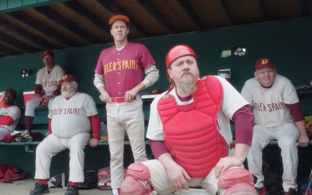 Film still from EEPHUS: A group of men of different ages, all wearing baseball uniforms, are watching a game.