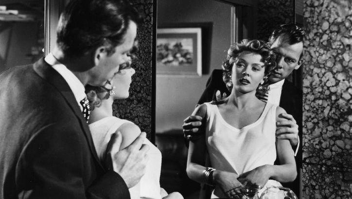 Film still from THE BIG HEAT: A man and a woman look at themselves in the mirror. He stands behind her and holds her by the arms.