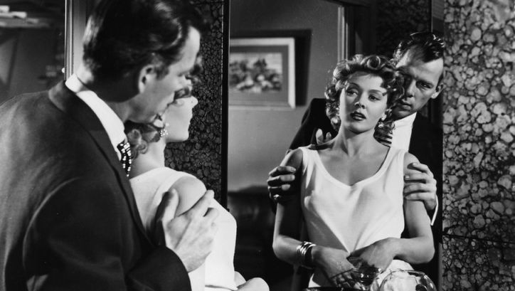 Filmstill aus THE BIG HEAT: Ein Mann und eine Frau betrachten sich im Spiegel. Er steht hinter ihr und hält sie an den Armen.