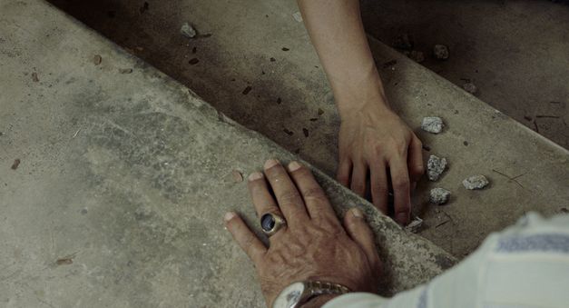 Film still from "Oasis of Now" by Chee Sum Chia. It shows a close-up of two hands on a concrete staircase. 