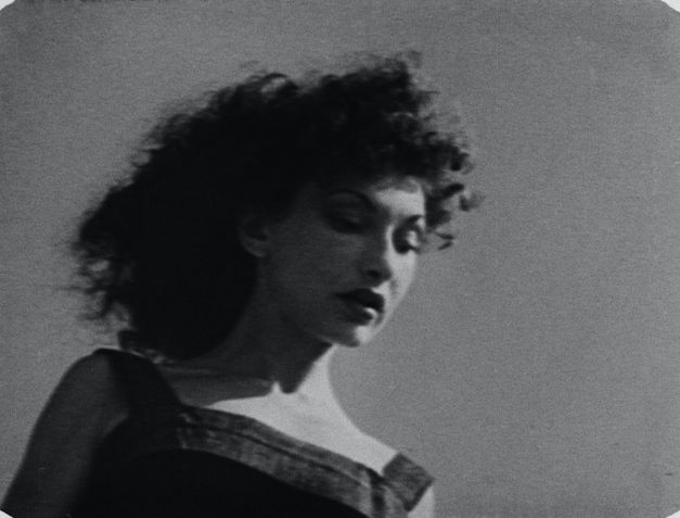 Film still from AT LAND: Black and white photo of a woman with dark curls, taken slightly below her head.