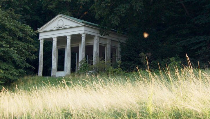 Filmstill from „De Facto" by Selma Doborac. A building with columns at the edge of a forest.