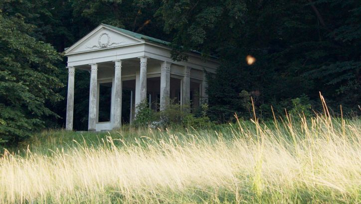 Filmstill from „De Facto" by Selma Doborac. A building with columns at the edge of a forest.