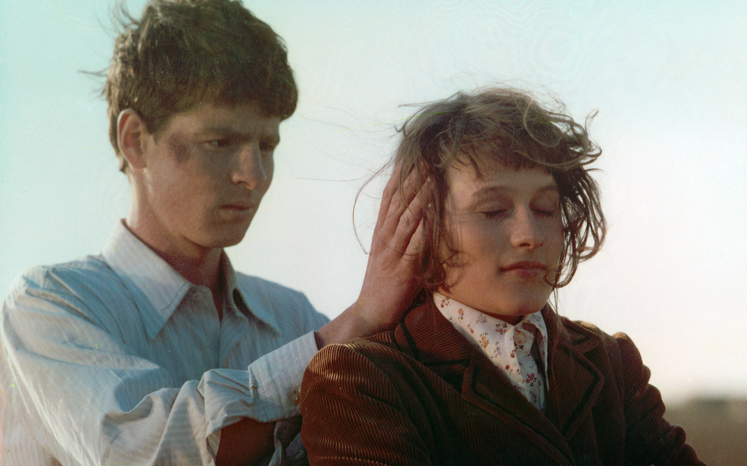 Filmstill aus ROMANZE MIT AMÉLIE: Ein junger Mann steht hinter einer jungen Frau und legt seine Hände an ihre Ohren.
