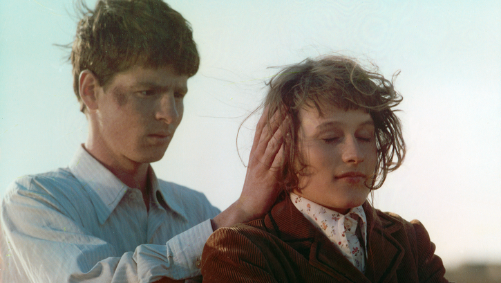 Filmstill aus ROMANZE MIT AMÉLIE: Ein junger Mann steht hinter einer jungen Frau und legt seine Hände an ihre Ohren. 