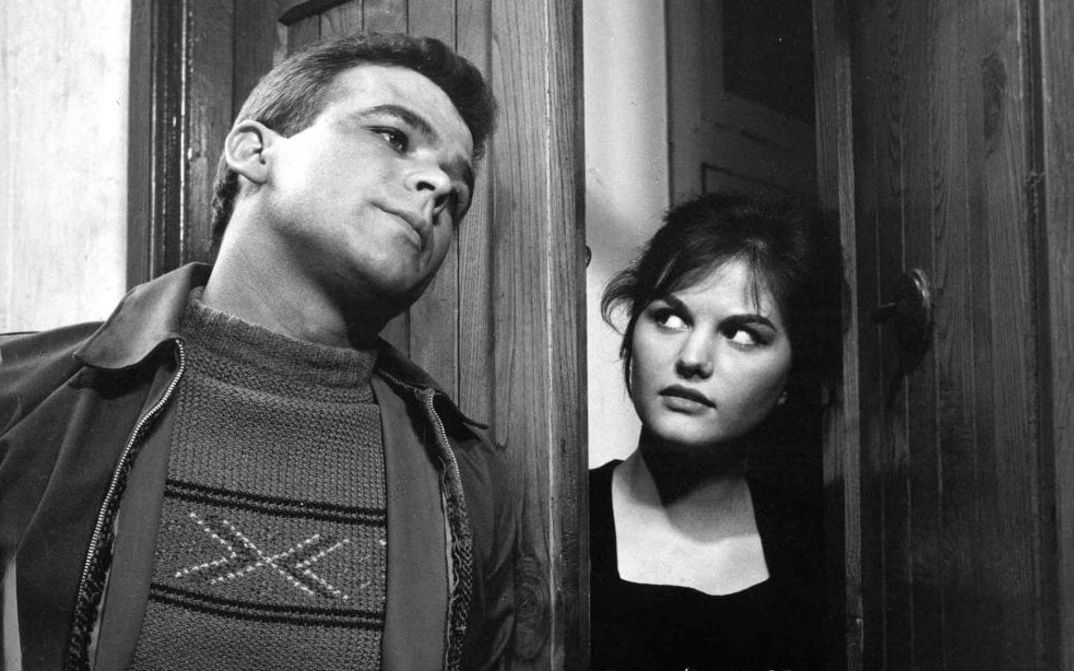 Film still from I SOLITI IGNOTI: A young man and a young woman are leaning against a door frame, she is looking at him sideways.