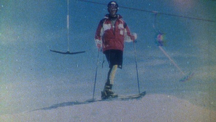 Film still from SCHUSS!: Photograph of a skier in front of a T-bar lift. The image is grainy.