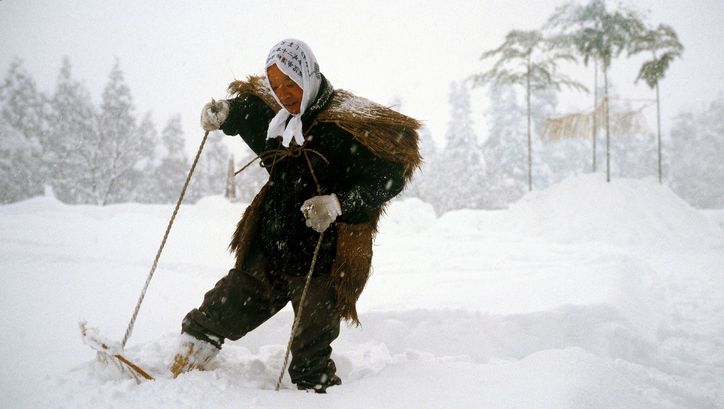 Film still from UNTER SCHNEE: A person in a historical costume walks with snowshoes through a snowy landscape.