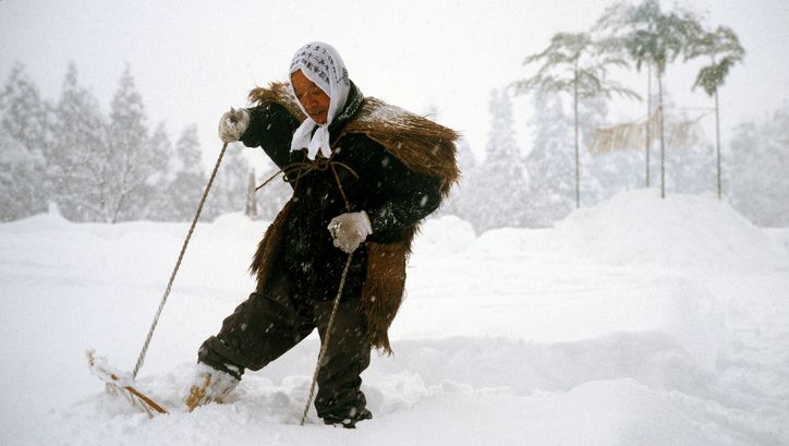 Film still from UNTER SCHNEE: A person in a historical costume walks with snowshoes through a snowy landscape.