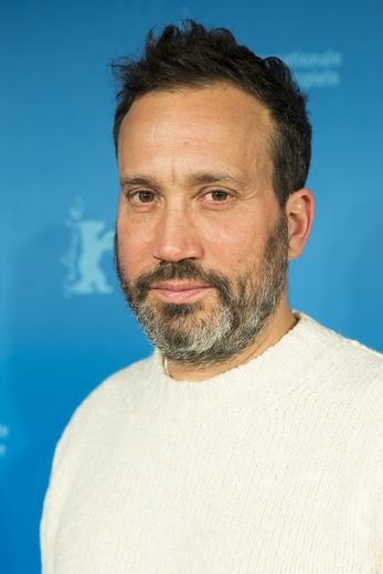 Portrait photo of a man looking into the camera. Behind him, we can see the blue Berlinale wall with the festival